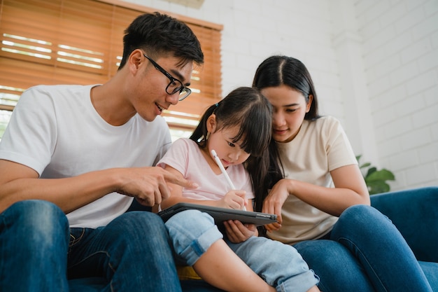 Szczęśliwy azjatycki rodzinny tata, mama i córka, siedząc na sofie w salonie w domu za pomocą technologii tabletu komputerowego