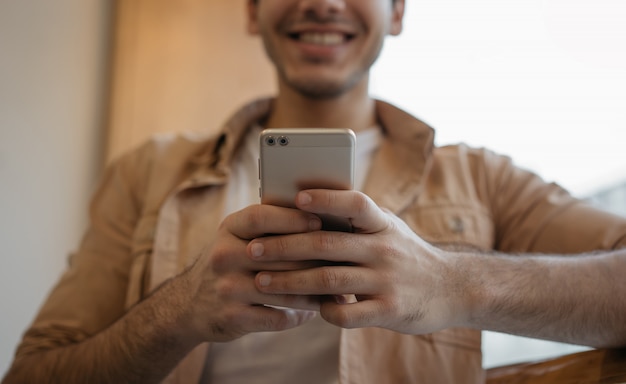 Szczęśliwy azjatykci mężczyzna mienia telefon komórkowy, gawędzenie, otrzymywa wiadomość tekstową, rezerwuje bilety, skupia się na rękach