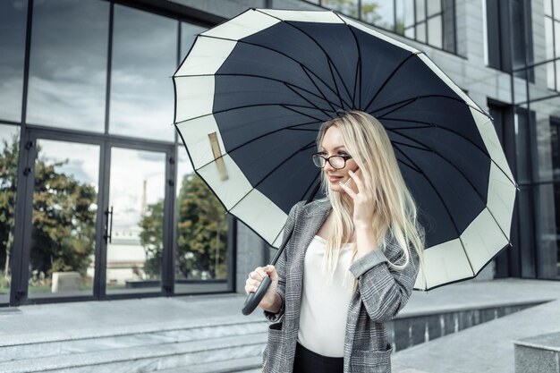 Szczęśliwy biznes kobieta hplding parasol i rozmawia przez telefon na tle biura firmy. Czekam na deszcz