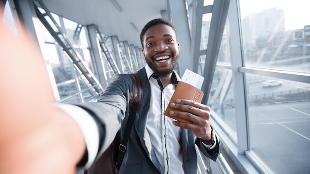 Szczęśliwy biznesmen afro biorący selfie na lotnisku posiadający paszport