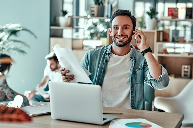 Szczęśliwy biznesmen rozmawia przez telefon komórkowy w kawiarni Uśmiechnięty mężczyzna pracujący z dokumentami i laptopem