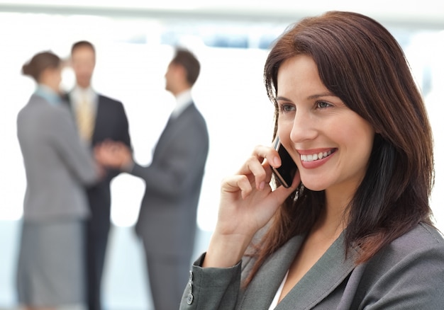 Szczęśliwy bizneswoman na telefonie podczas gdy jej drużyna pracuje