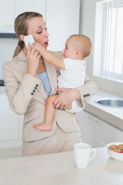 Szczęśliwy bizneswoman trzyma jej dziecka opowiada na telefonie