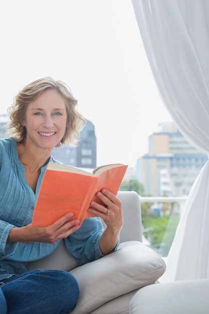 Szczęśliwy blondynki kobiety obsiadanie na jej leżance trzyma książkę
