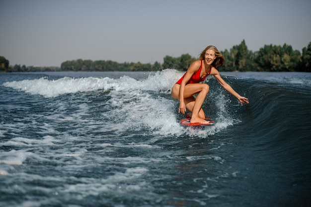 Szczęśliwy blondynki kobiety surfingowiec jedzie w dół błękitną chełbotanie macha