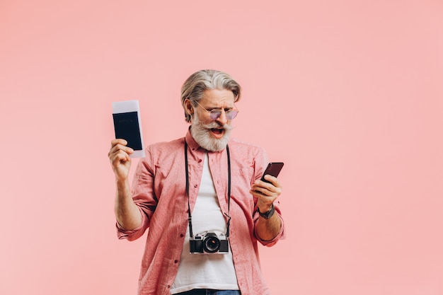 Szczęśliwy brodaty mężczyzna trzyma telefon komórkowego i paszport z biletami na menchiach w okularach przeciwsłonecznych