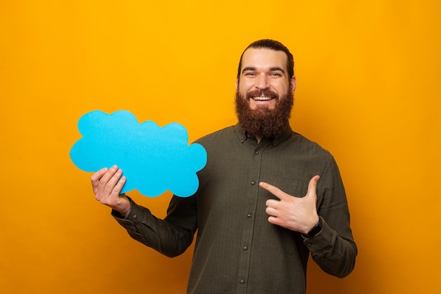 Szczęśliwy brodaty mężczyzna wskazuje na niebieski dymek w kształcie chmurki