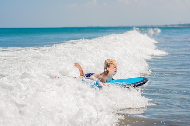 Szczęśliwy chłopczyk - młody surfer jeździć na desce surfingowej z zabawą na falach morskich. Aktywny rodzinny styl życia, lekcje sportów wodnych na świeżym powietrzu dla dzieci i pływanie na obozie surfingowym. Letnie wakacje z dzieckiem