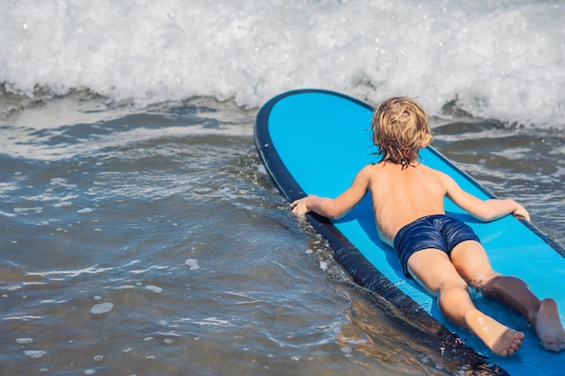 Szczęśliwy chłopczyk - młody surfer jeździć na desce surfingowej z zabawą na falach morskich. Aktywny rodzinny styl życia, lekcje sportów wodnych na świeżym powietrzu dla dzieci i pływanie na obozie surfingowym. Letnie wakacje z dzieckiem