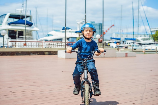 Szczęśliwy chłopiec bawi się w pobliżu klubu jachtowego z rowerem w piękny dzień Aktywne dziecko w kasku rowerowym