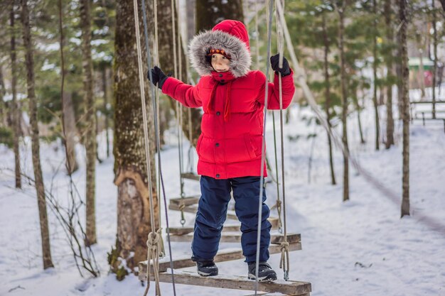 Szczęśliwy chłopiec cieszący się aktywnością we wspinaczkowym parku rozrywki w zimowy dzień