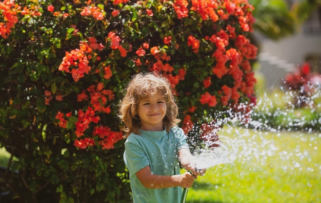 Szczęśliwy chłopiec nalewa wodę z węża dziecko podlewa kwiaty w ogrodzie przydomowym ogrodnictwie