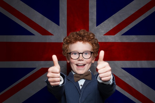 Zdjęcie szczęśliwy chłopiec pokazujący kciuk na tle brytyjskiej flagi naucz się angielskiego to fajne