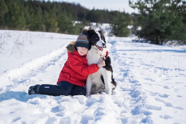 Szczęśliwy Chłopiec W Czerwonej Kurtce Bawiący Się Z Border Collie Na świeżym Powietrzu Na Tle Zimy