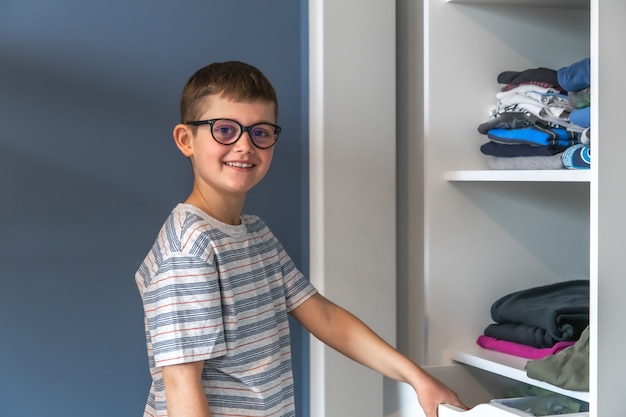 Szczęśliwy chłopiec w okularach stoi przy szafie i zastanawia się, w co się ubrać.