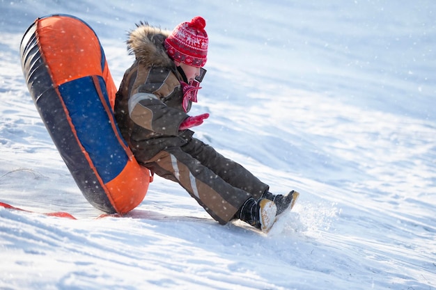Szczęśliwy chłopiec wzbija się w powietrze na rurce na sankach w śniegu Chłopiec zjeżdża zimą ze wzgórza