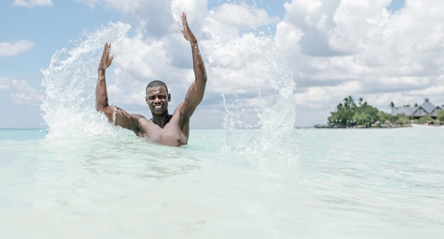 Szczęśliwy czarny człowiek bawi się wodą morską