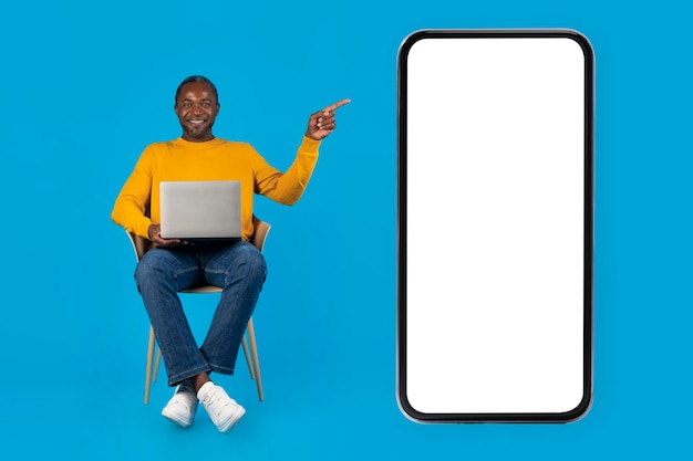 Szczęśliwy czarny człowiek używający komputera wskazującego na makieta smartfona