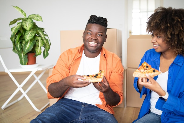 Szczęśliwy czarny mężczyzna i kobieta jedzą pizzę i świętują dzień przeprowadzki
