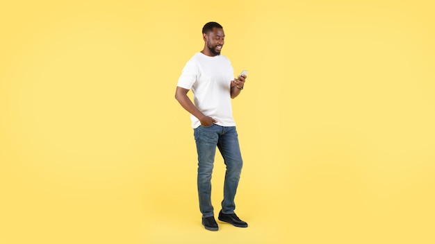Szczęśliwy czarny mężczyzna korzystający z telefonu stojącego na żółtym tle panoramy