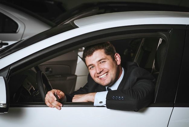 Szczęśliwy człowiek kupuje nowy samochódMłody biznesmen wybiera drogiego SUV-a w salonie samochodowym