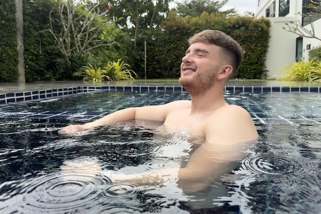 Szczęśliwy człowiek, młody, pozytywny facet, cieszący się letnimi wakacjami w basenie na podwórku domu, uśmiechając się
