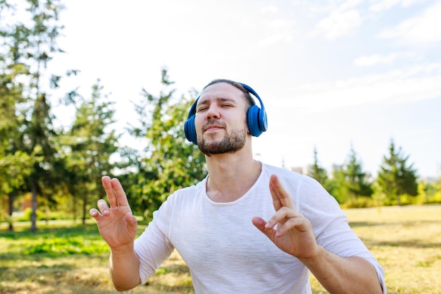 Szczęśliwy człowiek słuchania muzyki ze słuchawkami w białej marynarce na świeżym powietrzu w letnim parku