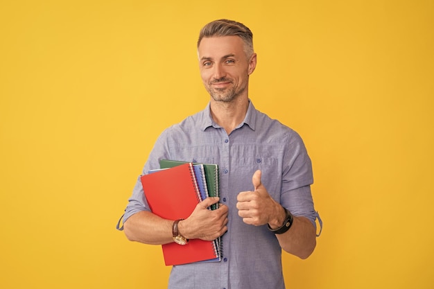 Szczęśliwy człowiek trzyma zeszyt szkolny lub planista pokazujący kciuk w górę edukacji