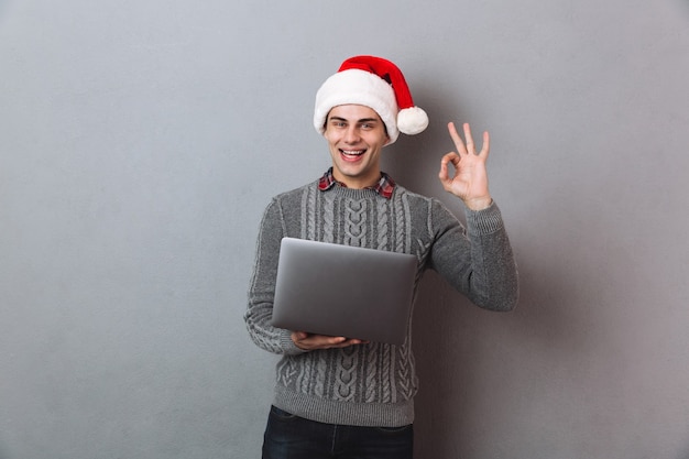 Szczęśliwy Człowiek W Sweter I Kapelusz Boże Narodzenie Trzymając Laptop I Pokazując Znak Ok