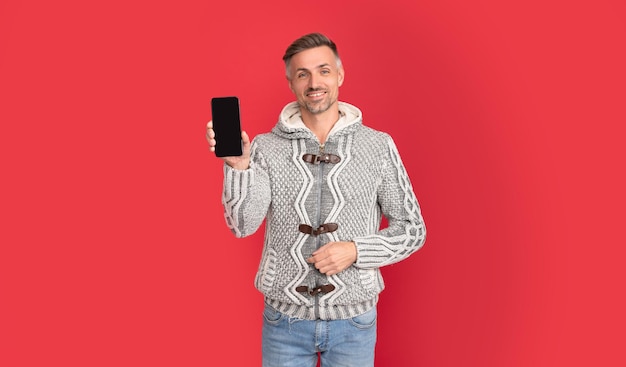 Szczęśliwy człowiek w swetrze pokazujący ekran telefonu na czerwonym tle z reklamą miejsca na kopię