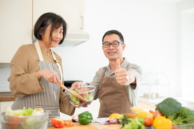 Szczęśliwy dorosły azjatycki mąż pokazuje kciuk do kamery podczas wspólnego gotowania w kuchni