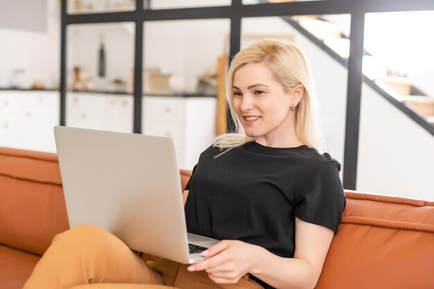 Szczęśliwy dorywczo piękna kobieta pracuje na laptopie, siedząc w domu.