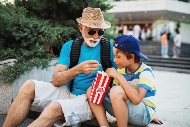 Szczęśliwy dziadek ciesząc się z wnukiem podczas jedzenia popcornu na zewnątrz na ulicy miasta.