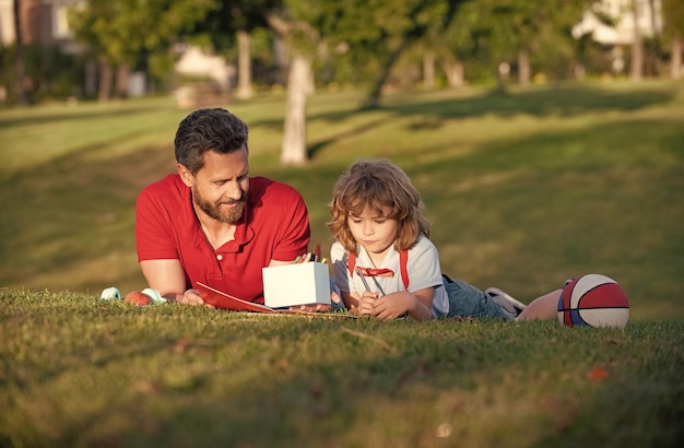 Szczęśliwy dzień ojca szczęśliwa rodzina tata i chłopiec dziecko relaksuje się na trawie w parku dziecko trzyma naukę rysowania