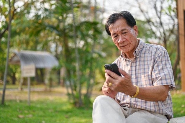 Szczęśliwy emeryt w wieku azjatyckim używający smartfona na podwórku