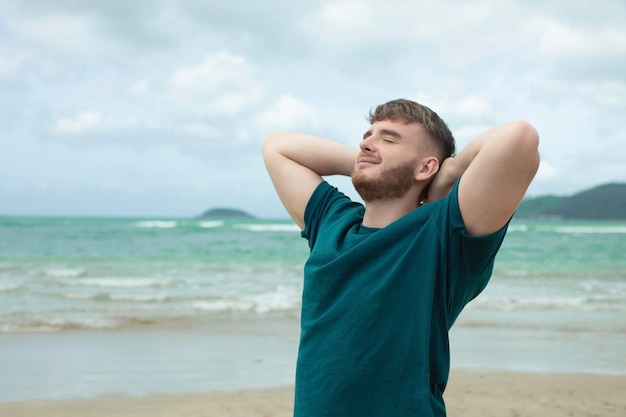 Szczęśliwy facet, młody przystojny mężczyzna, cieszy się wakacjami na plaży morskiej w tropikalnym egzotycznym kraju, uśmiechając się, dobrze się bawiąc