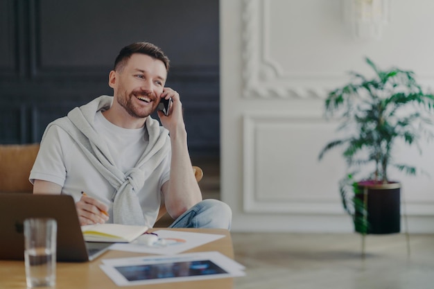 Szczęśliwy freelancer rozmawiający przez telefon siedzący przy biurku w domowym biurze