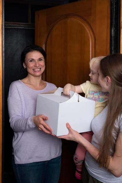 Szczęśliwy gość przyniósł pudełko ciasta Młoda matka i dziecko witają gościa prezentem