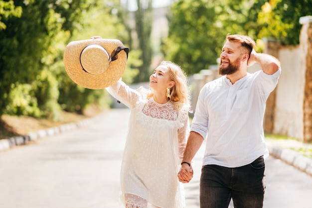 Szczęśliwy i roześmiany mężczyzna i kobieta trzymając się za ręce idąc drogą w słoneczny dzień
