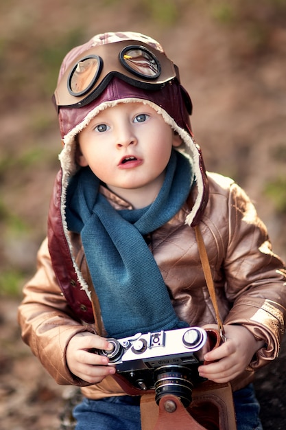 Szczęśliwy i stylowy chłopak z aparatem w rękach w skórzanej brązowej kurtce z zabawkowym miodem pitnym