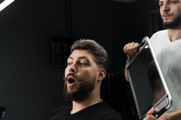 Zdjęcie szczęśliwy i zaskoczony brodaty mężczyzna patrząc w lustro w salonie fryzjerskim. pokazuje efekt słabego blaknięcia włosów maszynowych.