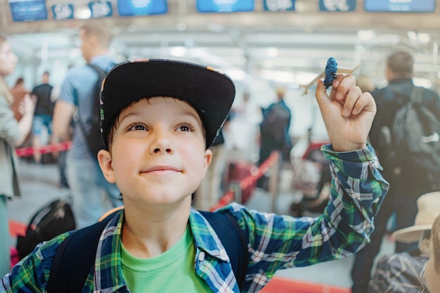 szczęśliwy kaukaski chłopiec przed podróżą samolotem trzymający zabawkowy samolot w hali lotniska przed odlotem