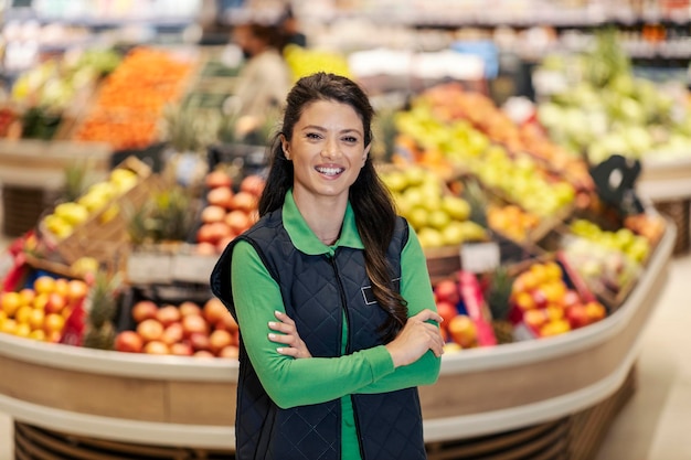 Szczęśliwy kierownik sprzedaży stoi z rękami skrzyżowanymi w supermarkecie i uśmiecha się do kamery