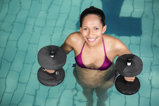 Szczęśliwy kobieta w ciąży ćwiczy w basenie z ciężarami przy centrum wolnego czasu