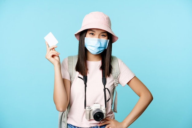 Szczęśliwy koreański turysta, dziewczyna na wakacjach stojąca z kartą kredytową i aparatem, płacąca za pamiątki, podróżująca za granicę, stojąca na niebieskim tle