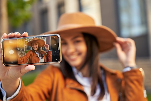 Szczęśliwy ładna młoda dama w kapeluszu co selfie podczas pozowanie w mieście. Koncepcja stylu życia