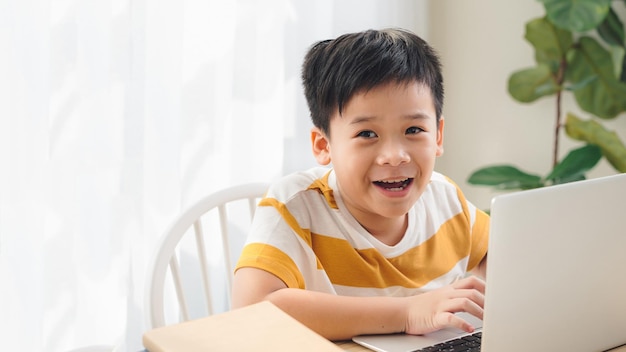 Szczęśliwy ładny mały chłopiec w szkole odrabiania lekcji i używania laptopa w domu