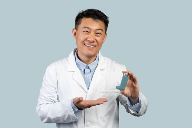 Szczęśliwy lekarz azjatycki mężczyzna w średnim wieku w białym fartuchu pokazuje inhalator do opieki zdrowotnej