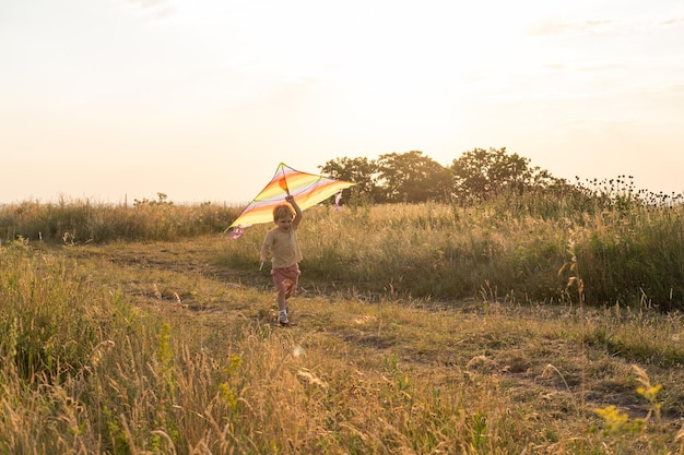 Szczęśliwy mały chłopiec bawi się latawcem w przyrodzie o zachodzie słońca