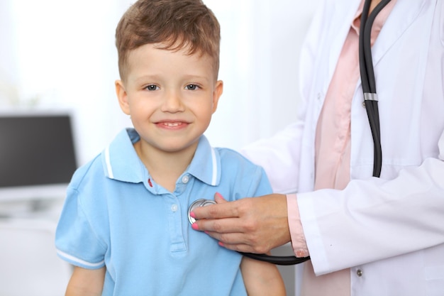Szczęśliwy mały chłopiec bawi się podczas badania przez lekarza stetoskopem